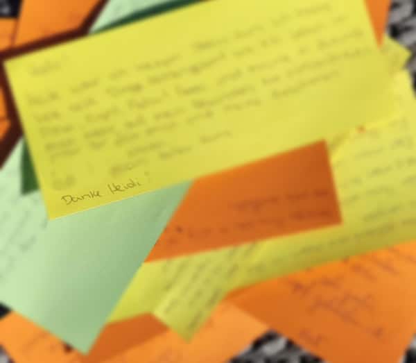 Blurred close-up of overlapping yellow, orange, and pastel sticky notes with handwritten messages.